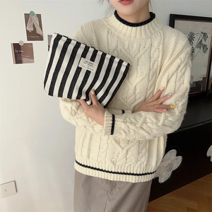 Close-up of black and white striped canvas toiletry bag held by a person in a cozy setting