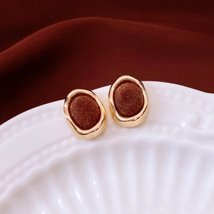 Close-up of vintage gold rimmed earrings with dark brown flocking on a white ceramic plate