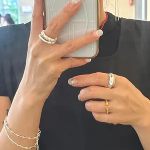 Close-up of minimalist layered silver rings and thin bead bracelet in mirror selfie