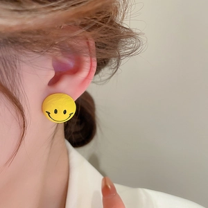 Close-up of a model wearing a cute yellow smiley face stud earring with silver needles
