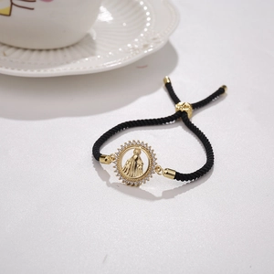 Detail of a gold plated Virgin Mary pendant on a black woven adjustable bracelet
