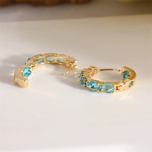Elegant gold earrings with light blue zircon stones in a circular design on a bright surface