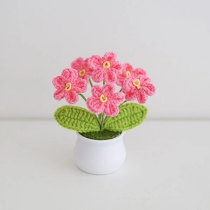 Close-up of handmade pink crochet flowers with yellow stamens in a white ceramic pot