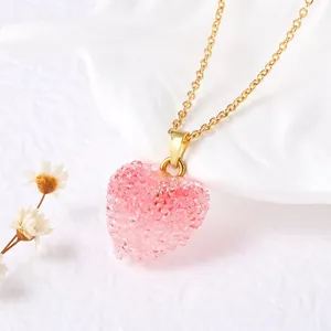 Gros plan d'un collier avec pendentif coeur en cristal rose et chaîne dorée texturée