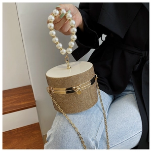 Detailed close-up of golden cylindrical evening bag with rhinestones and pearl handle