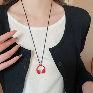 Close-up of a vibrant red headphone pendant necklace worn over a white and black outfit