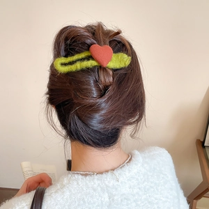 Close-up of a green plush hair clip with a red heart detail styled in a hair bun