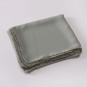 Macro detail of grey-green satin scarf featuring elegant golden bead chain trim edge
