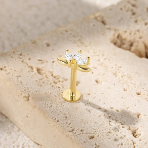 Detail of a golden lotus stud earring with clear gems on a textured beige stone surface