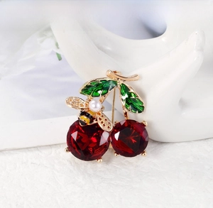 Close-up of cherry brooch with red crystal fruits, green enamel leaf and tiny pearl bee