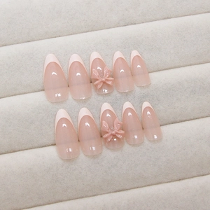 Pink almond press-on nails with white French tips and 3D bow accents on a velvet display