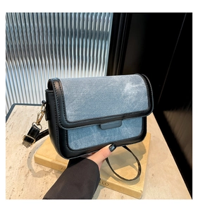 Close-up of light blue denim crossbody bag with black trim and gold hardware details