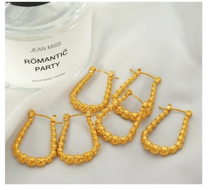 Close-up of golden beaded U-shaped earrings on white silk fabric with mirror highlights