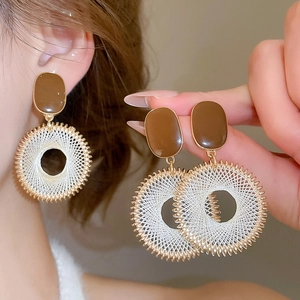Detail view of bohemian enamel circle earrings with cream woven texture and golden base