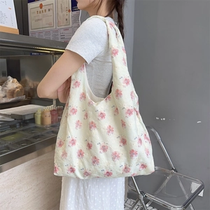 Detail of floral embroidery on cream canvas tote bag worn by a female model