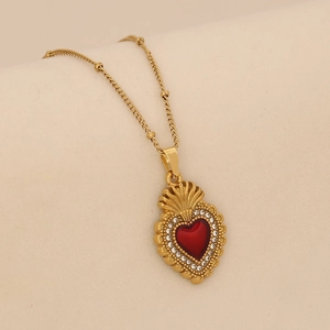 Gros plan d'un collier doré avec pendentif cœur en émail rouge et cristaux brillants