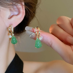 Detail of gold hoop earrings with green gourd pendants and shimmering cubic zirconia stones