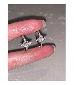Close-up of silver star hoop earrings with sparkling zircon stones held by fingers
