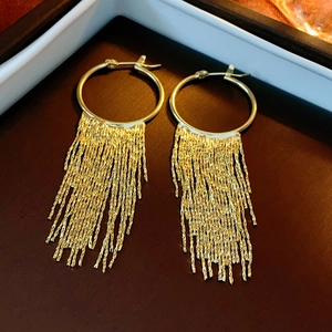 Close-up of golden tassel hoop earrings showing intricate metal texture and polished finish