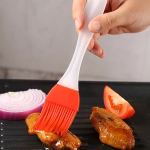 Silicone BBQ brush with red head applying sauce to grilled chicken wings on a tray