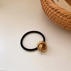 Detail of minimalist black elastic hair tie with gold woven metal knot decoration