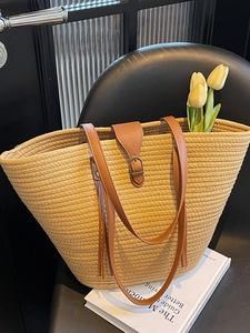 Large hand-woven straw tote bag with brown PU leather handles on a black chair