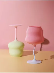 Artistic detail of wavy pastel glass wine goblets in pink and yellow with curved stems