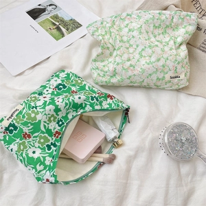 Green floral canvas makeup bags on a white textured cloth with beauty accessories