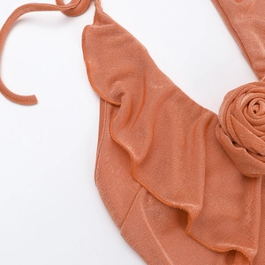 Detail of orange knit dress featuring a 3D rose accent and ruffled edges on fabric
