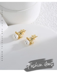 Detail of gold-plated bear earrings holding a white pearl on a minimalist stone background