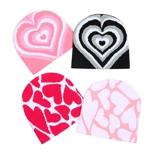 Detailed knit texture of four beanies with heart patterns in pink, black, and red colors