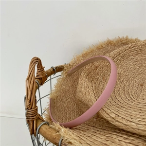 Detailed shot of a minimalist slim pink fabric headband leaning on a straw hat accessory