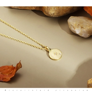 Close-up of gold coin necklace with starburst micro-inlaid zirconium on a stone background
