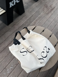 Close-up of cream canvas tote bag with black See Sea lettering on a wooden table