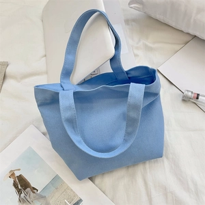 Flat lay of light blue canvas tote bag with laptop and magazine on white fabric