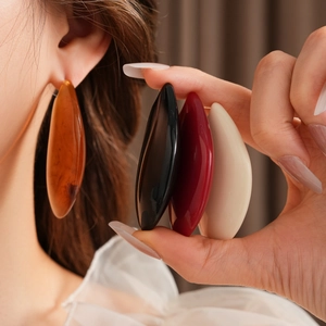 Détail de boucles d'oreilles géométriques en résine en ambre noir rouge et crème