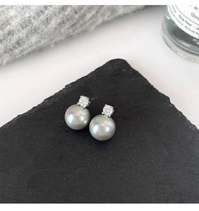 Close-up of elegant grey pearl stud earrings with zircon inlay on a dark stone surface