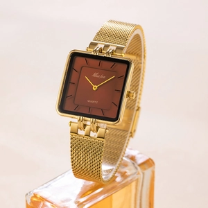 Detail view of square gold quartz watch with brown dial on a textured glass surface