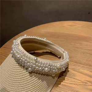 Detail of beige straw sun visor featuring elegant large white pearl embellishments