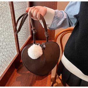 Detail einer dunkelbraunen herzförmigen Wildledertasche mit weißem Pompon-Anhänger