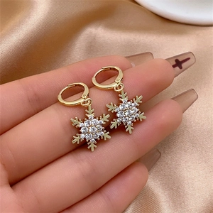 Detailed view of gold snowflake tassel earrings held by hand on champagne satin fabric