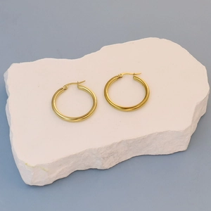 Polished gold flat round hoop earrings in stainless steel on white stone display