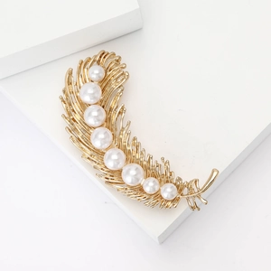 Elegant gold feather brooch featuring multiple white pearls on a minimalist white background