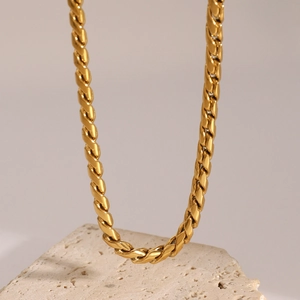 Macro shot of gold twist rope chain necklace draped on a beige textured stone block