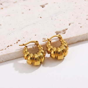 Macro shot of gold croissant hoop earrings with textured finish on stone pedestal