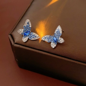 Primer plano de pendientes de mariposa con cristales azules sobre cuero oscuro