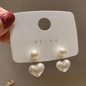 Elegant gold metal heart-shaped pearl earrings displayed on a white branded jewelry card