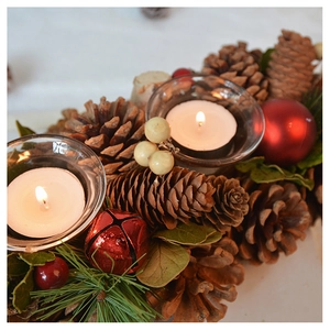 Close-up of pine cones, red ornaments, and evergreen branches around a candle
