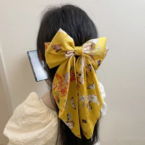 Close-up of yellow floral bow hair clip with long ribbons worn on model's hair