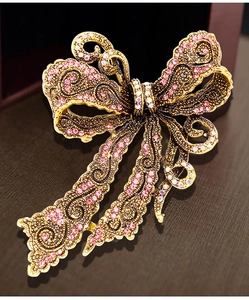 Close-up of vintage gold bow brooch with pink rhinestones and hollow patterns